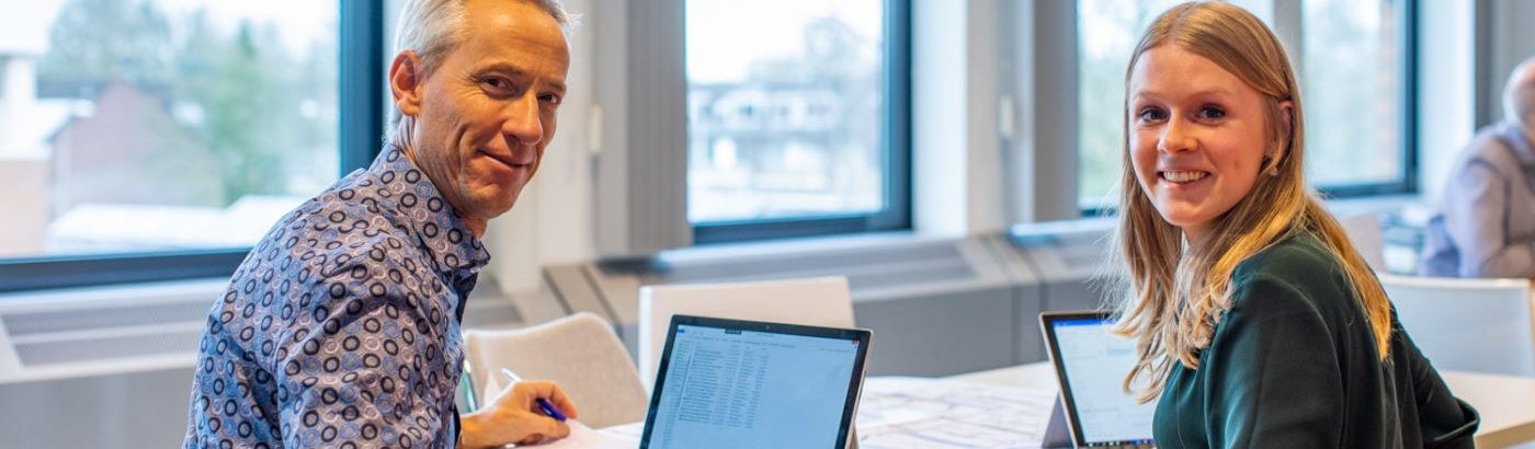 Man en vrouw zitten achter computer en draaien zich om naar de camera - Pijnacker